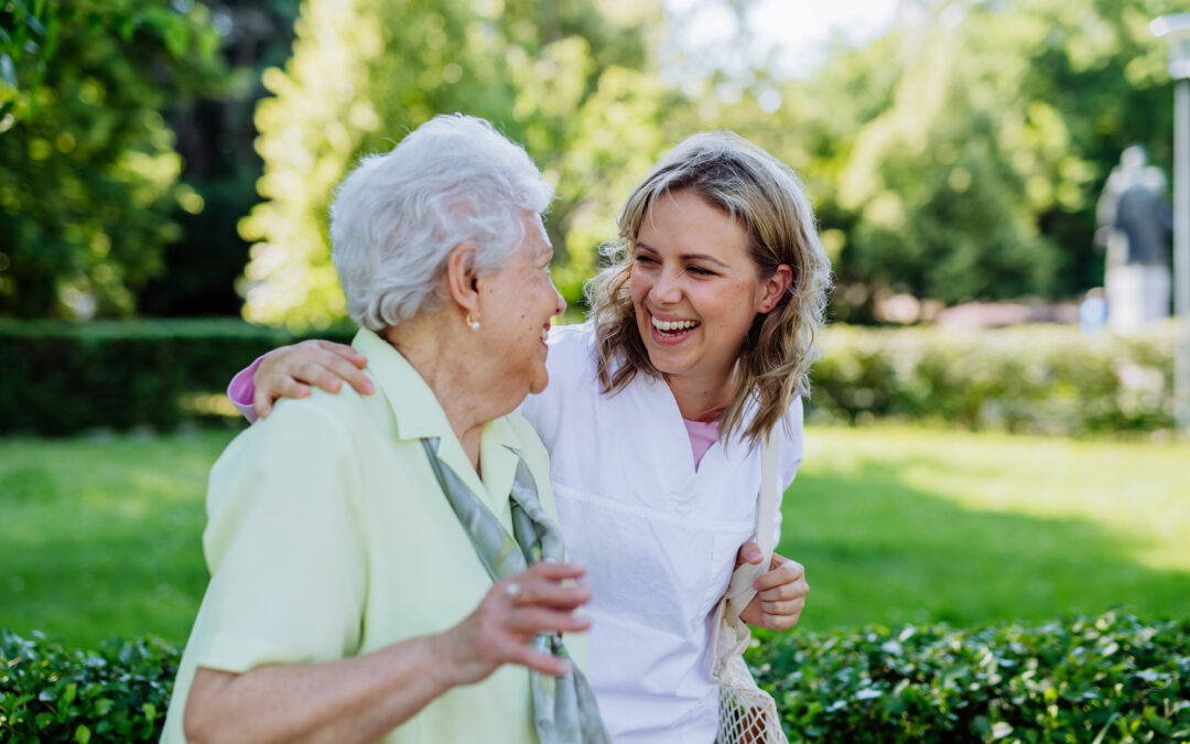 dwie kobiety w radosnych uśmiechach, na spacerze; opiekunka z seniorką